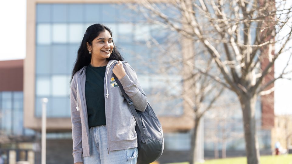 student standing outside Shineman Hall, gazing over their shoulder with a backpack on.