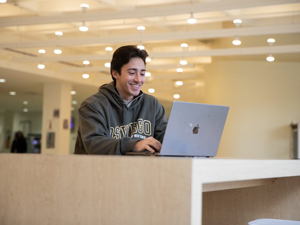 student sitting at a table smiling at their laptop.
