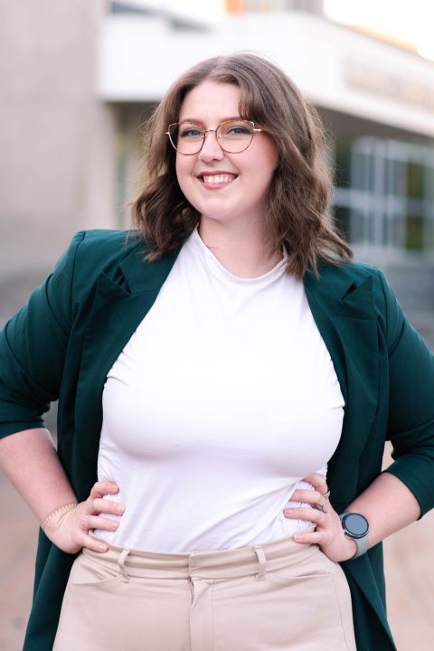 Maddy Knaack, standing outside with her hands on her hips, smiling