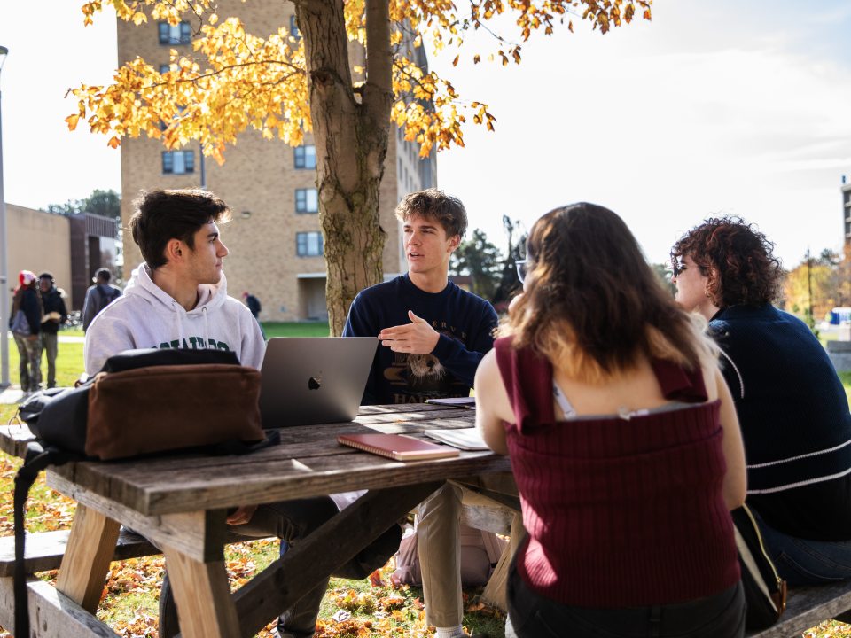 Students with laptops working outside at a picnic table.