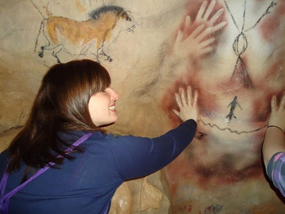 A student with her hand on a wall that that has cave drawings on it