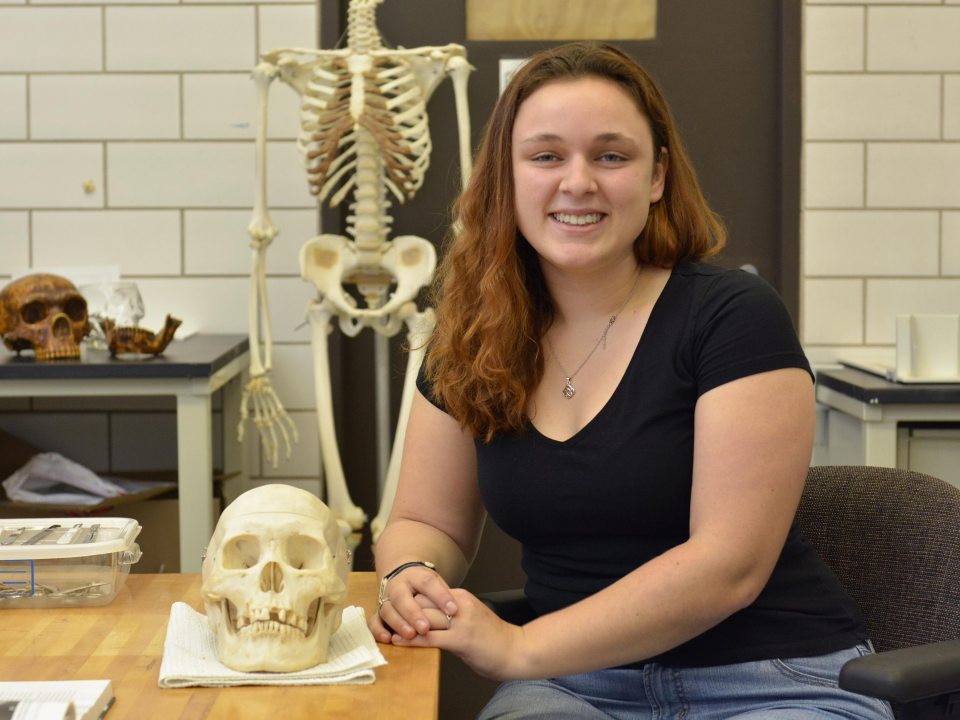 A student witting at a table next to a human skull
