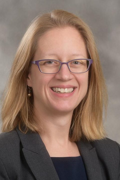 Professional headshot of a smiling woman with glasses and blonde hair.