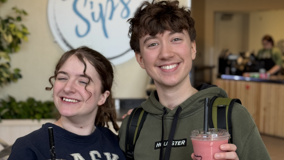 Two students holding their shakes form in front of the Sips sign