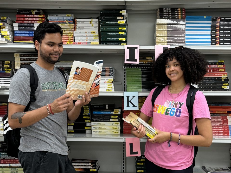 Students holding books in front of a shelf. 