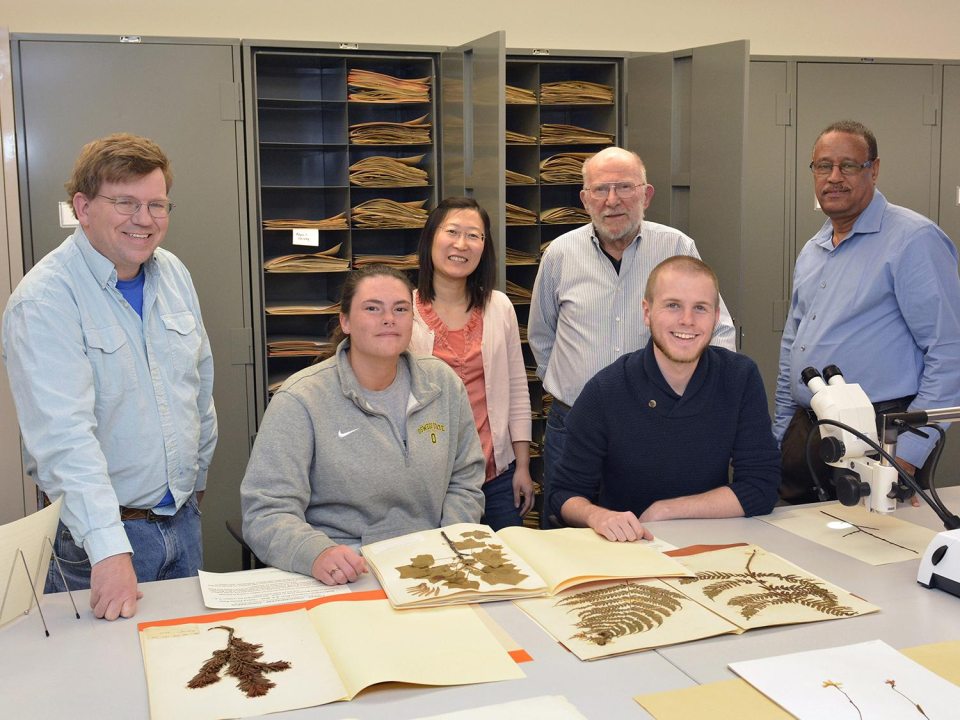 A group of people standing at a table with books of dried plant specimens