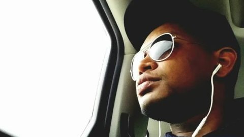 A student wearing sunglasses and earbuds, looking out the window of a vehicle