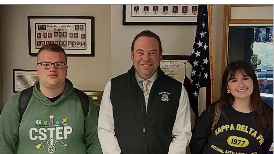 Three individuals stand together inside the SUNY Oswego University Police office. University Police Chief Scott Swayze stands in the center between Criminal Justice students Brandon Wilson and Val Di Marco following an interview discussion on crime theories and victimization for a CRJ 333 class project.