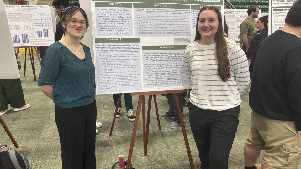 Two students stand beside their research poster at SUNY Quest 2026. Mikeal Halpainy-Livermore stands on the left and Laura Winfield stands on the right presenting their Criminal Justice research on the growing popularity of true crime media.