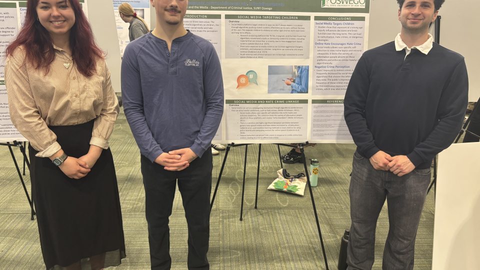 Three Criminal Justice students stand in front of their SUNY Quest 2026 research poster. From left to right are Nina Simmons, Jacob Johnston, and Tomer Zilberberg, presenting their project on how social media algorithms influence public exposure to crime-related content.
