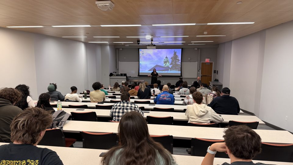 Students and faculty attend a Criminal Justice research panel in a SUNY Oswego classroom. Audience members are seated while student researchers present findings from projects examining crime, media, public perception, and contemporary criminal justice issues.