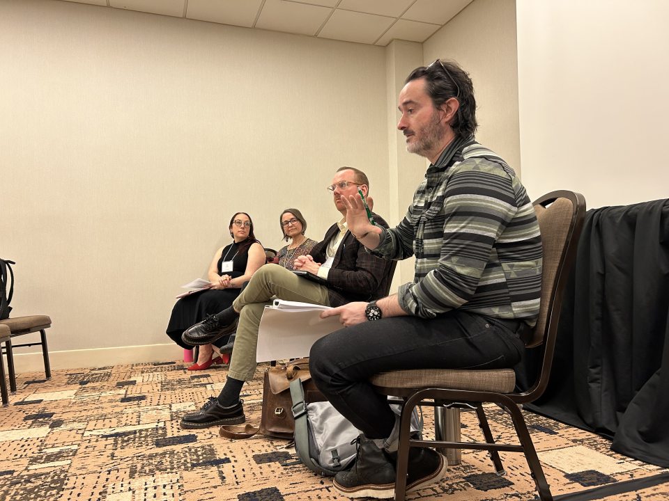 Dr. Matthew McLesky sitting with three fellow panelists at an academic conference, participating in a research panel discussion.
