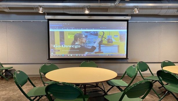 Photo of the South projector screen in the room including some chairs and tables.