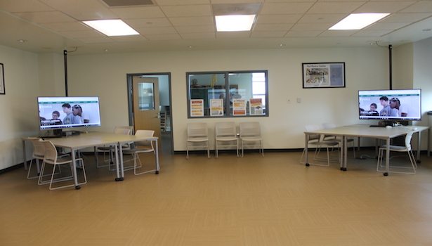 Photo of the back of the classroom from the center of the room. Including 2 student workstations and chairs.