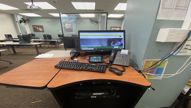 Photo of the podium showing the monitor, mouse/keyboard, phone PC and Blu-Ray player.