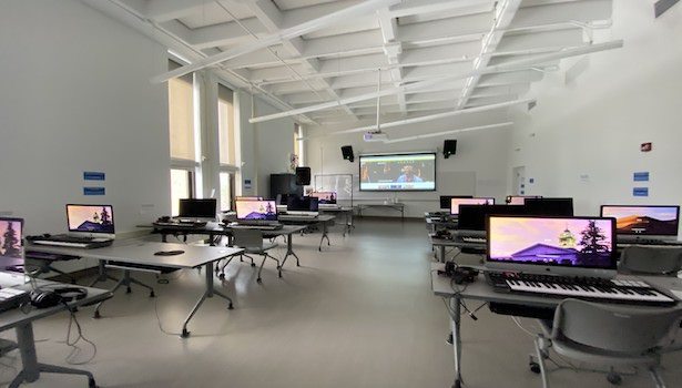 Photo of the front of the room from the back center. Showing podium, student chairs and projector screen