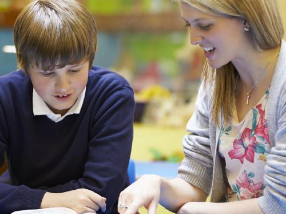 Student teacher guiding elementary student through a book