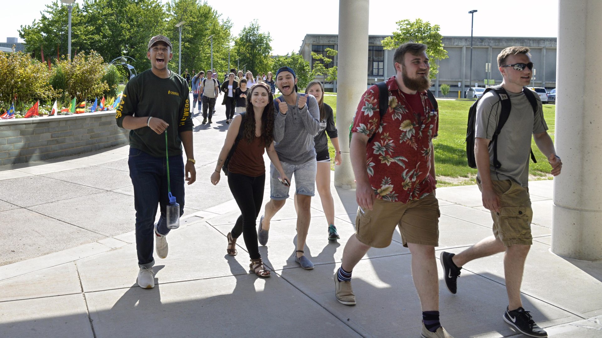 Laker Leaders walking into Marano Campus Center during Orientation on a bright and sunny day. They are looking towards the camera smiling.