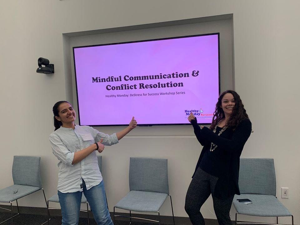 2 women smiling and pointing at their Destress for Success slide on a projection screen