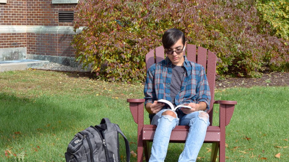 Student reading in Adirondack chair on quad.