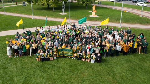 Large group of faculty, staff, and students supporting Oswego by wearing green and gold and waving green and gold flags