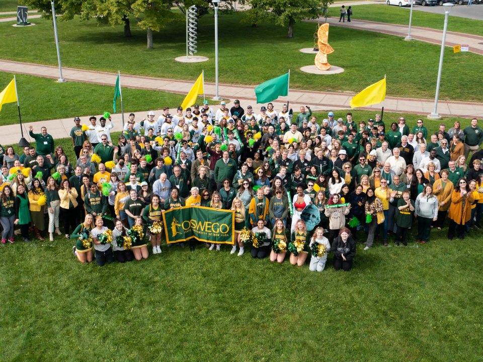 Large group of faculty, staff, and students supporting Oswego by wearing green and gold and waving green and gold flags
