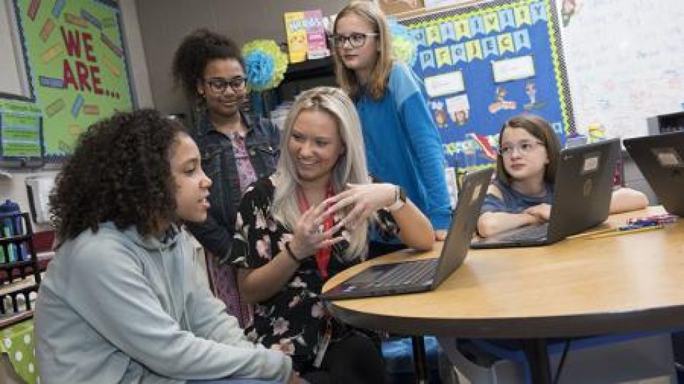 A teacher sitting at a table with 4 young girls of various ethnicities
