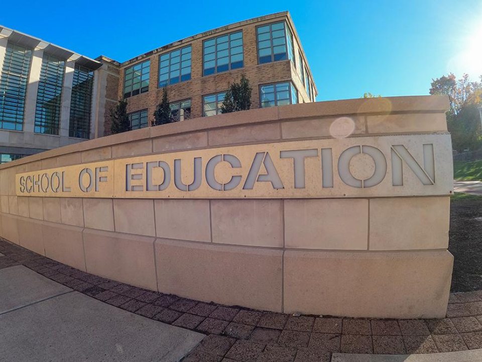 Building exterior with &#039;School of Education&#039; sign under a clear blue sky.