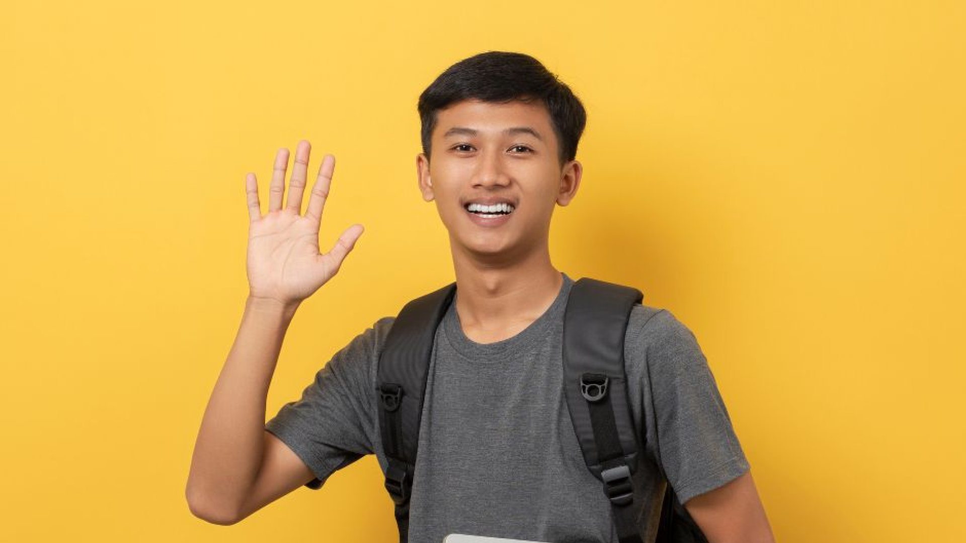 Student waving while holding books