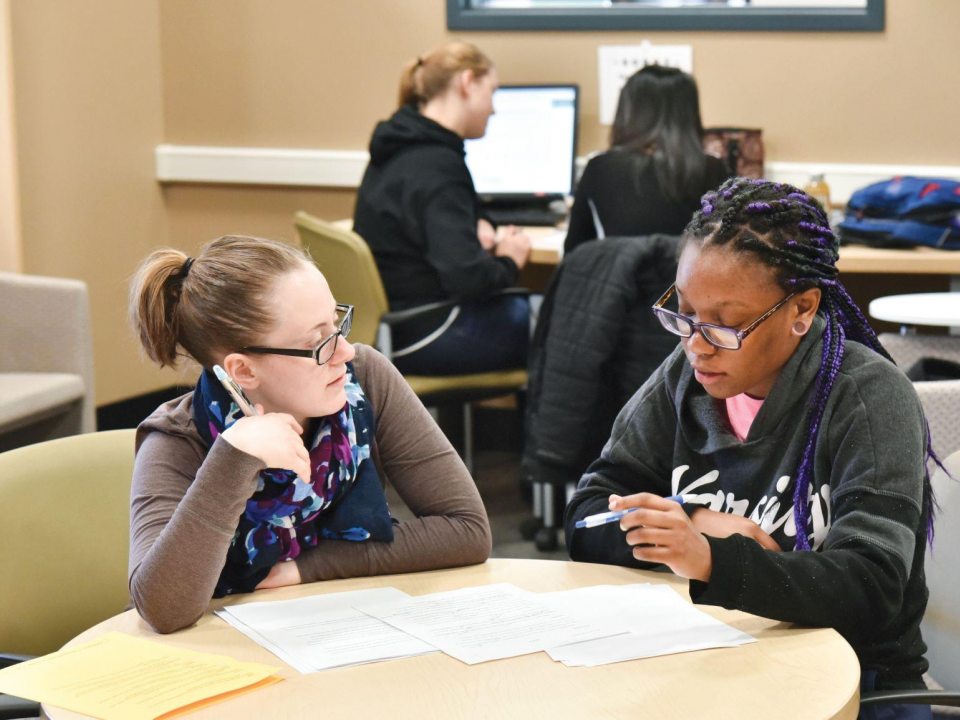 two female students sitting at a table with papers in front of them