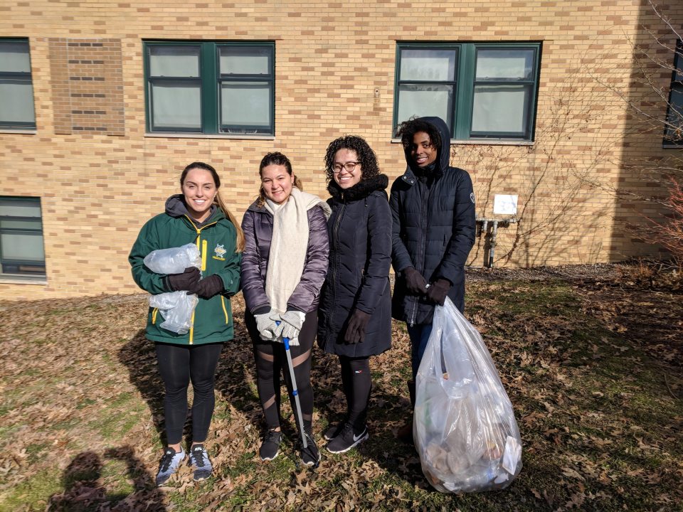 A group of students standing in front of a building, holding a filled garbage bag
