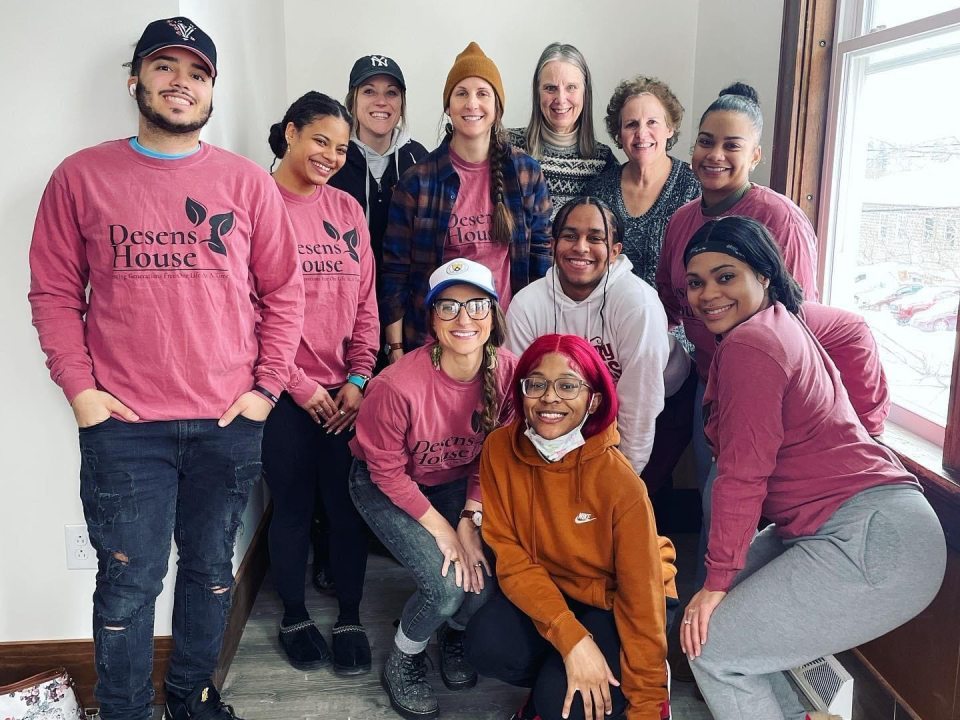 A group of students smiling at the camera, some of whom are wearing pink shirts that say Desens House