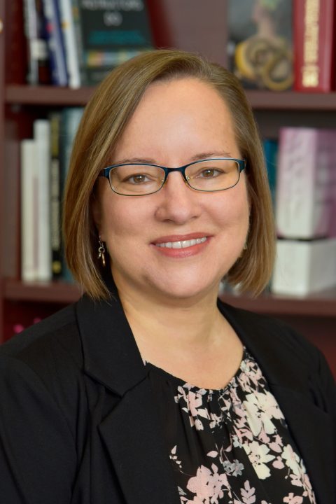 Kristen Croyle Portrait against a bookshelf with books