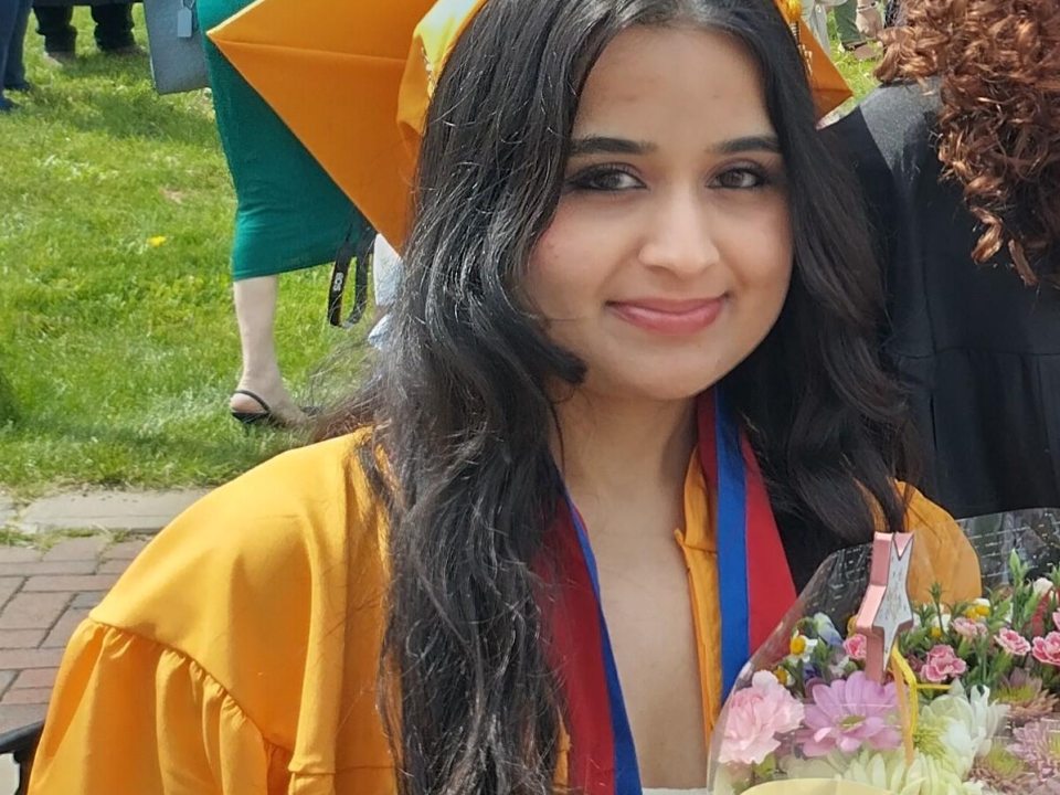 A GWS Student at Graduation Dressed in a Gold Cap and Gown Holding Flowers