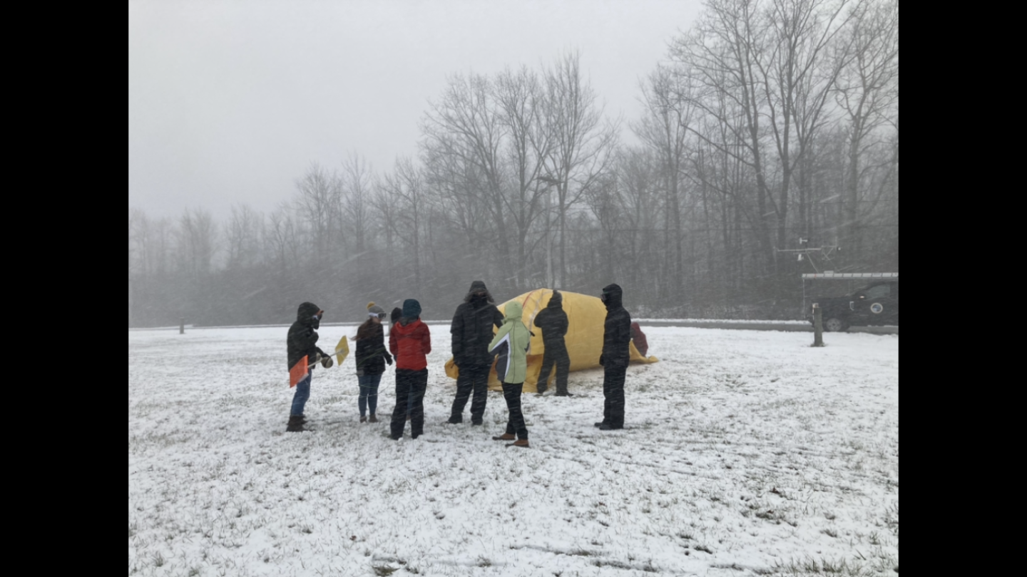 People wearing winter jackets gathered in front of a weather balloon on the ground