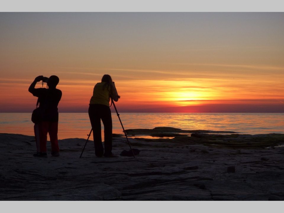 Two photographers taking photos of the sunset over Lake Ontario, reflecting the importance of preserving the Great Lakes’ natural and cultural heritage.