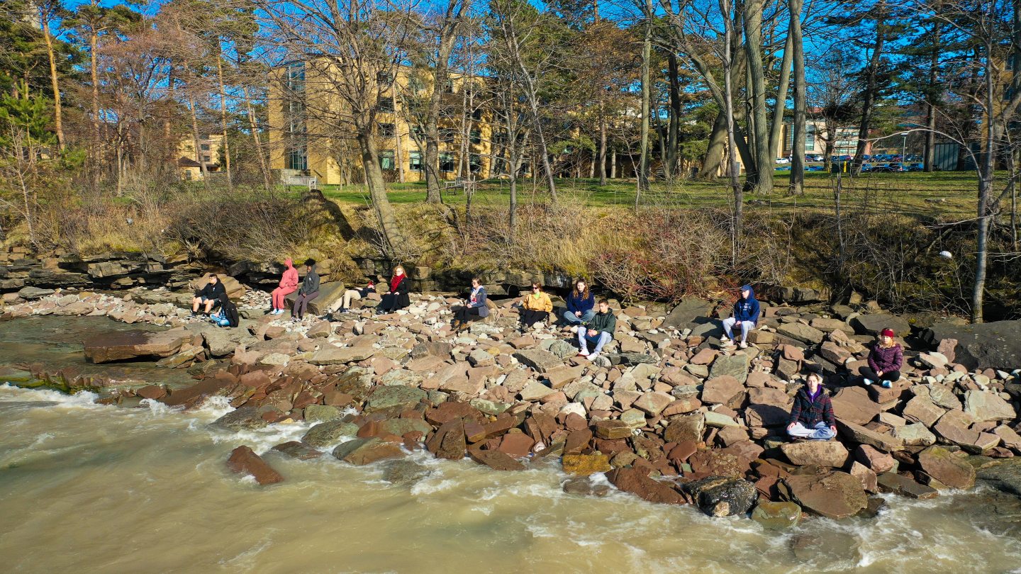 Aerial view of yoga students sitting on rocks of the shoreline