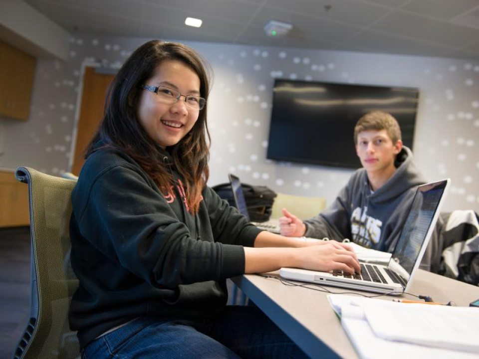 Two students working on laptops in a study room.