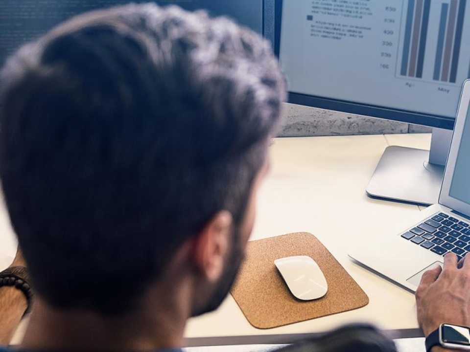 A person working on a laptop while looking at data on multiple monitors.