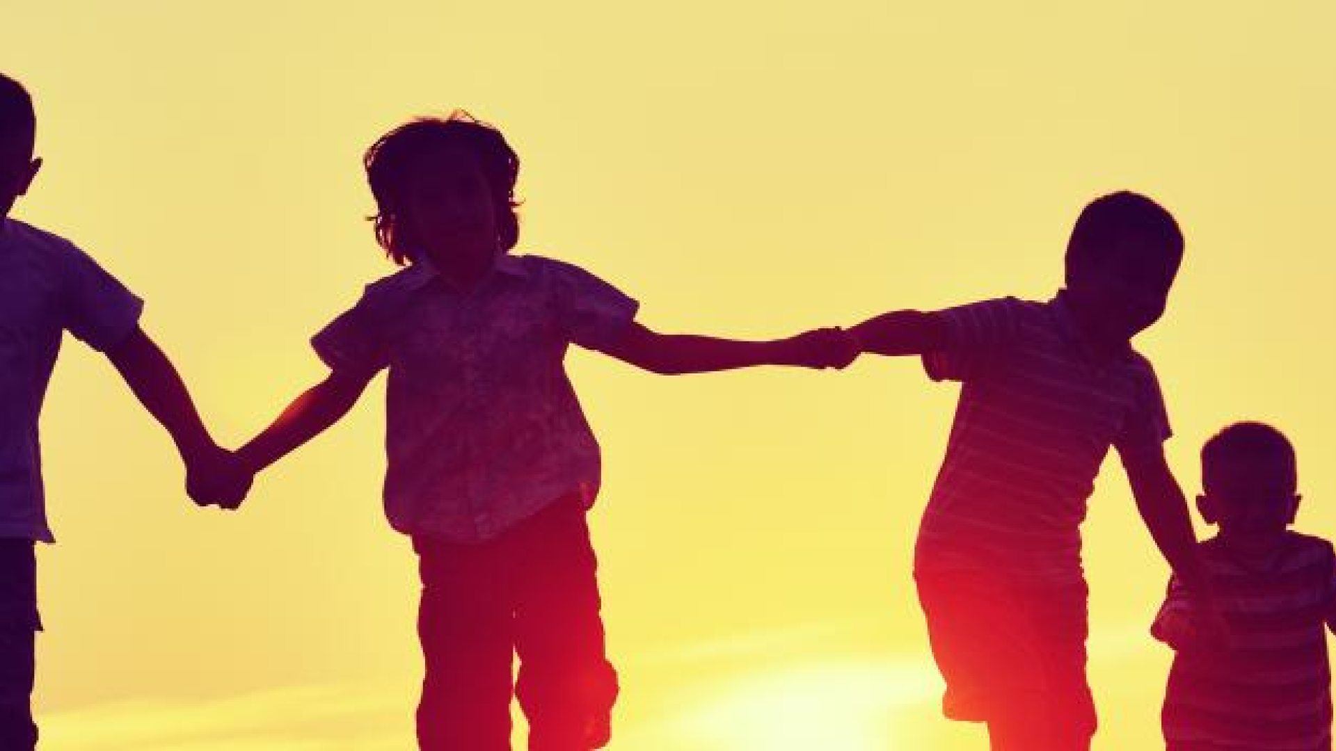 Silhouette of six children holding hands at sunset.
