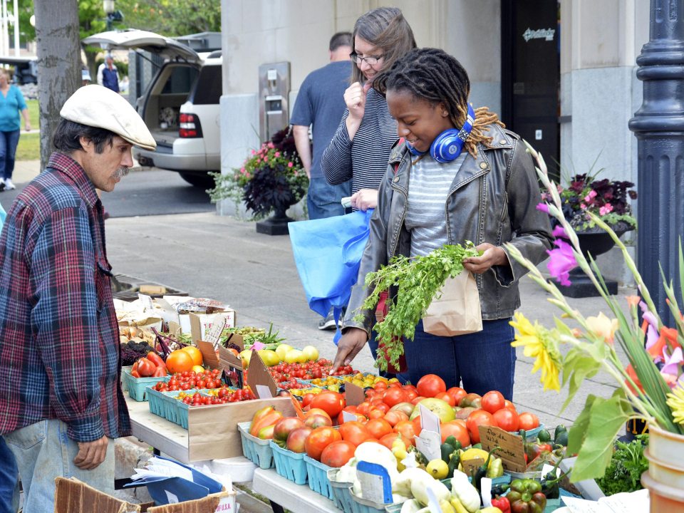 People at a farmer&#039;s market, looking at a table of produce
