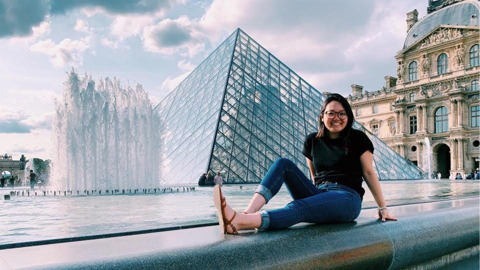 A woman sitting next to a fountain outside the Louvre Museum
