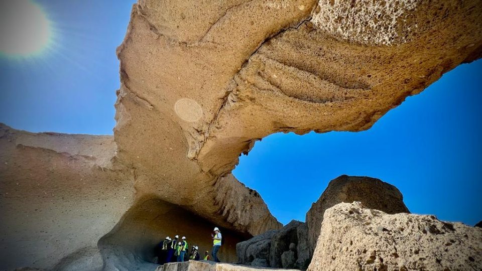 People Walking Under Rock Formation