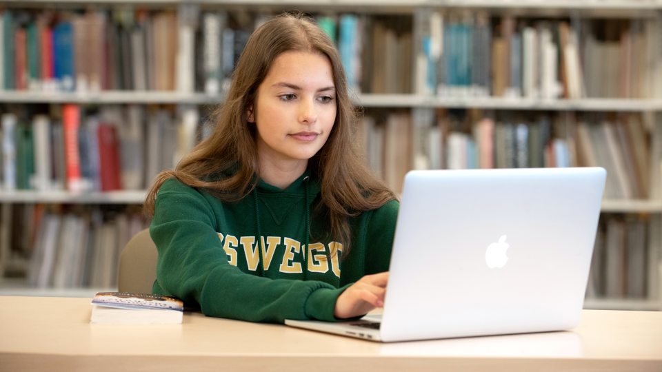 Student in Oswego Sweatshirt Typing on Computer