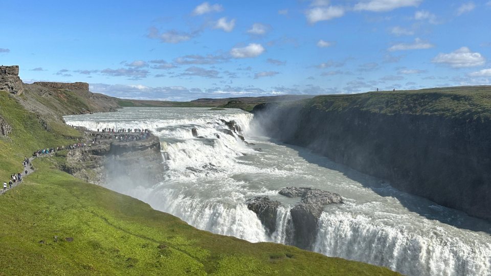 Wide view of Gullfoss waterfall in Iceland with green hills and a bright blue sky