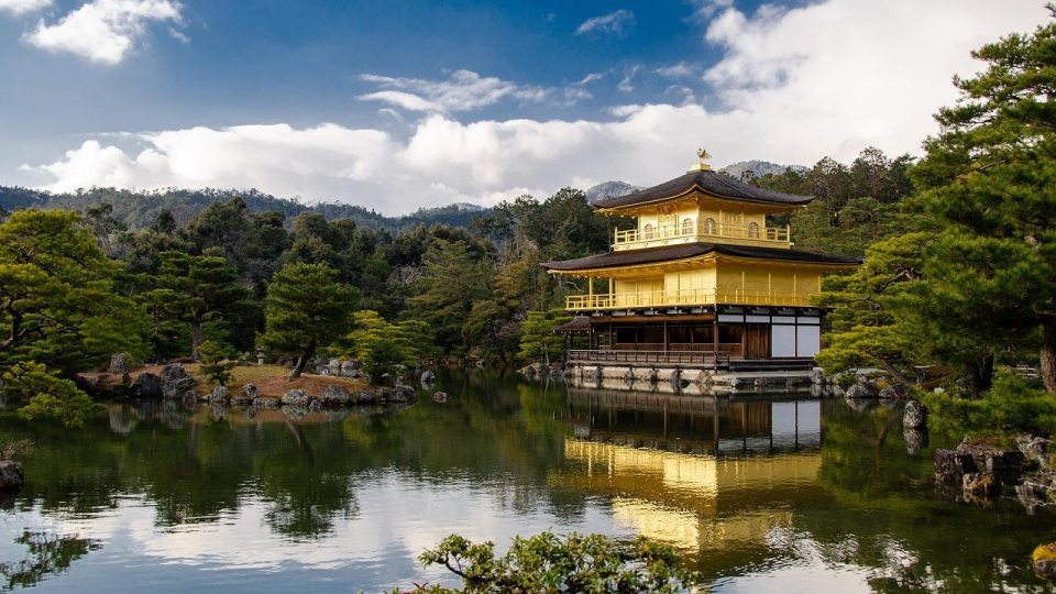 Golden Pavilion temple in Kyoto, Japan, reflected in a pond surrounded by trees and mountains