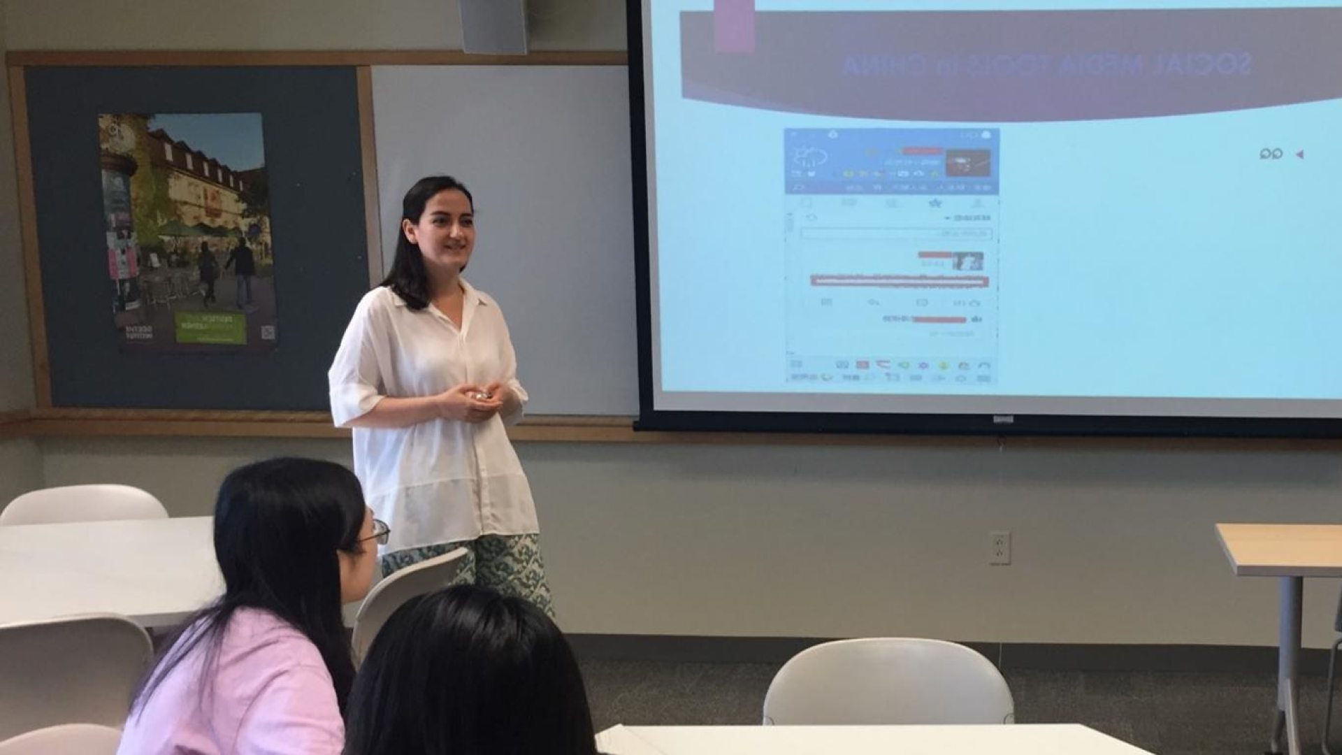 A woman standing in front of a projection screen showing a slide presentation