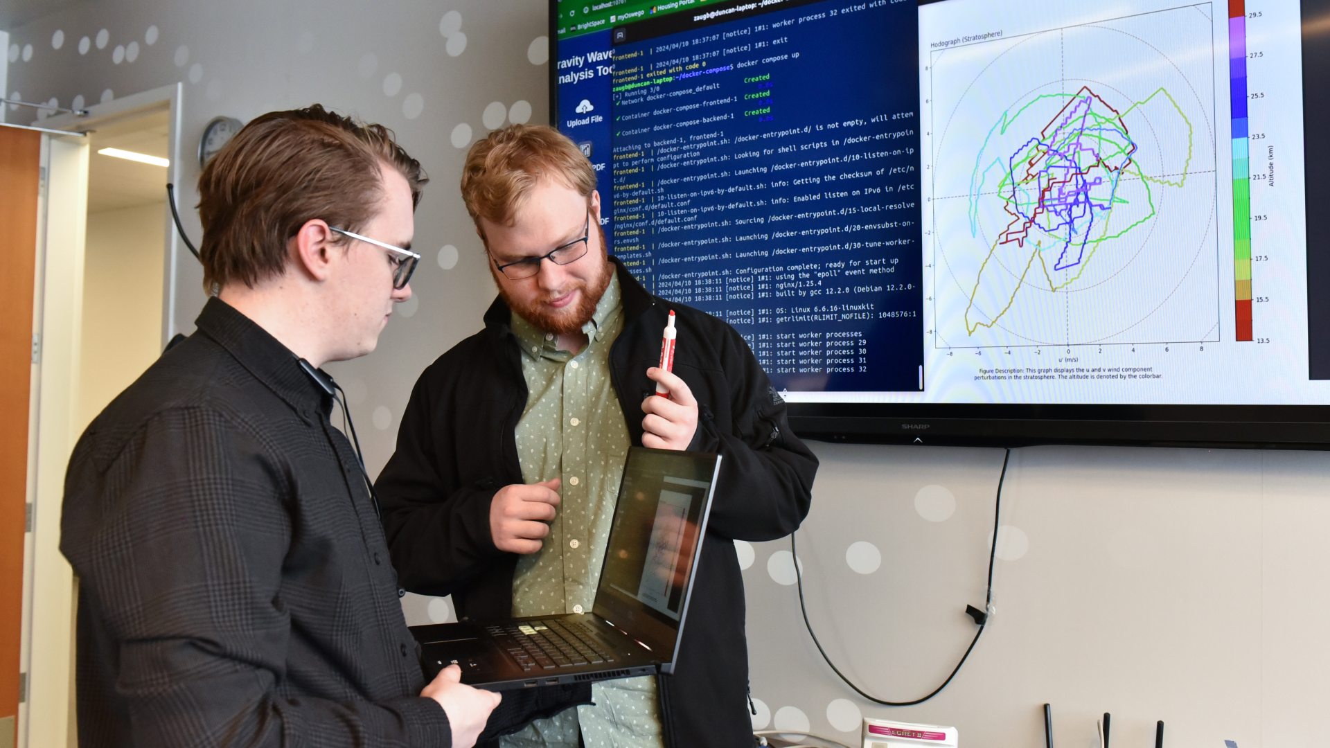 Two students review code and data visualizations on a screen while working together on a computer science project.