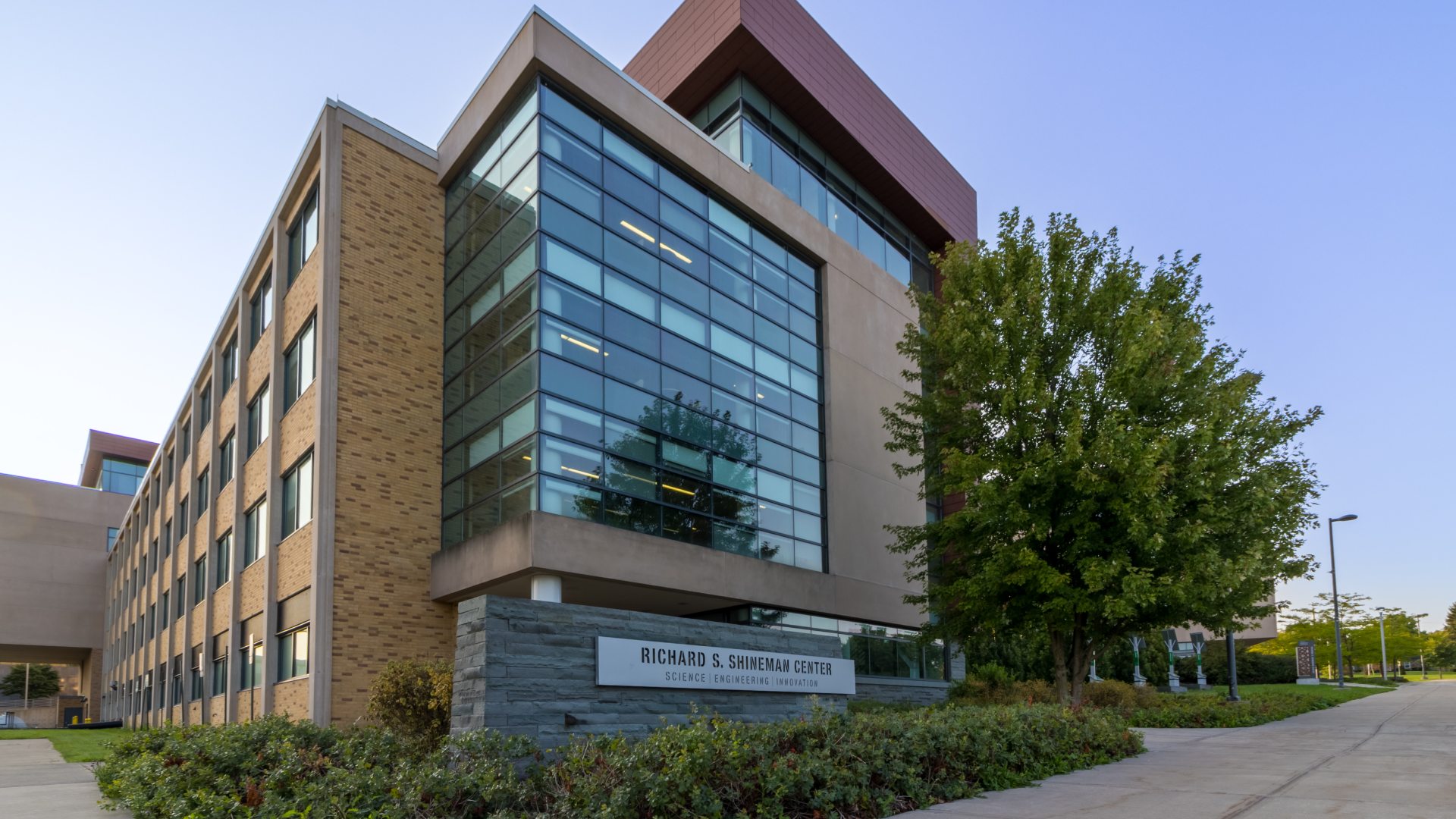 Exterior view of the Richard S. Shineman Center for Science, Engineering and Innovation at SUNY Oswego, featuring modern glass architecture and surrounding greenery.