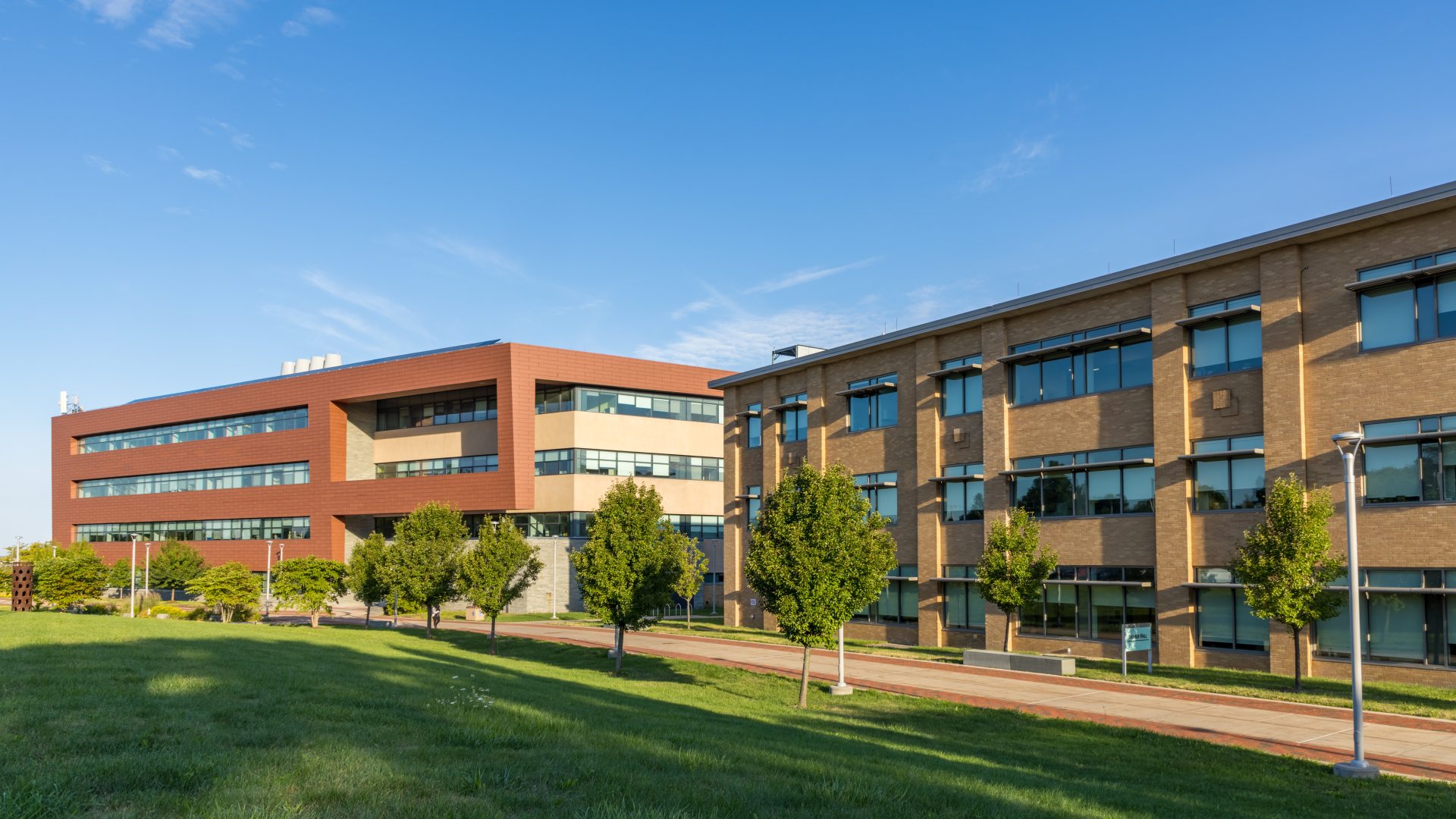 The Richard S. Shineman Center stands on SUNY Oswego’s campus, featuring modern architecture, solar panels, and a prominent vertical sign in a landscaped green space.
